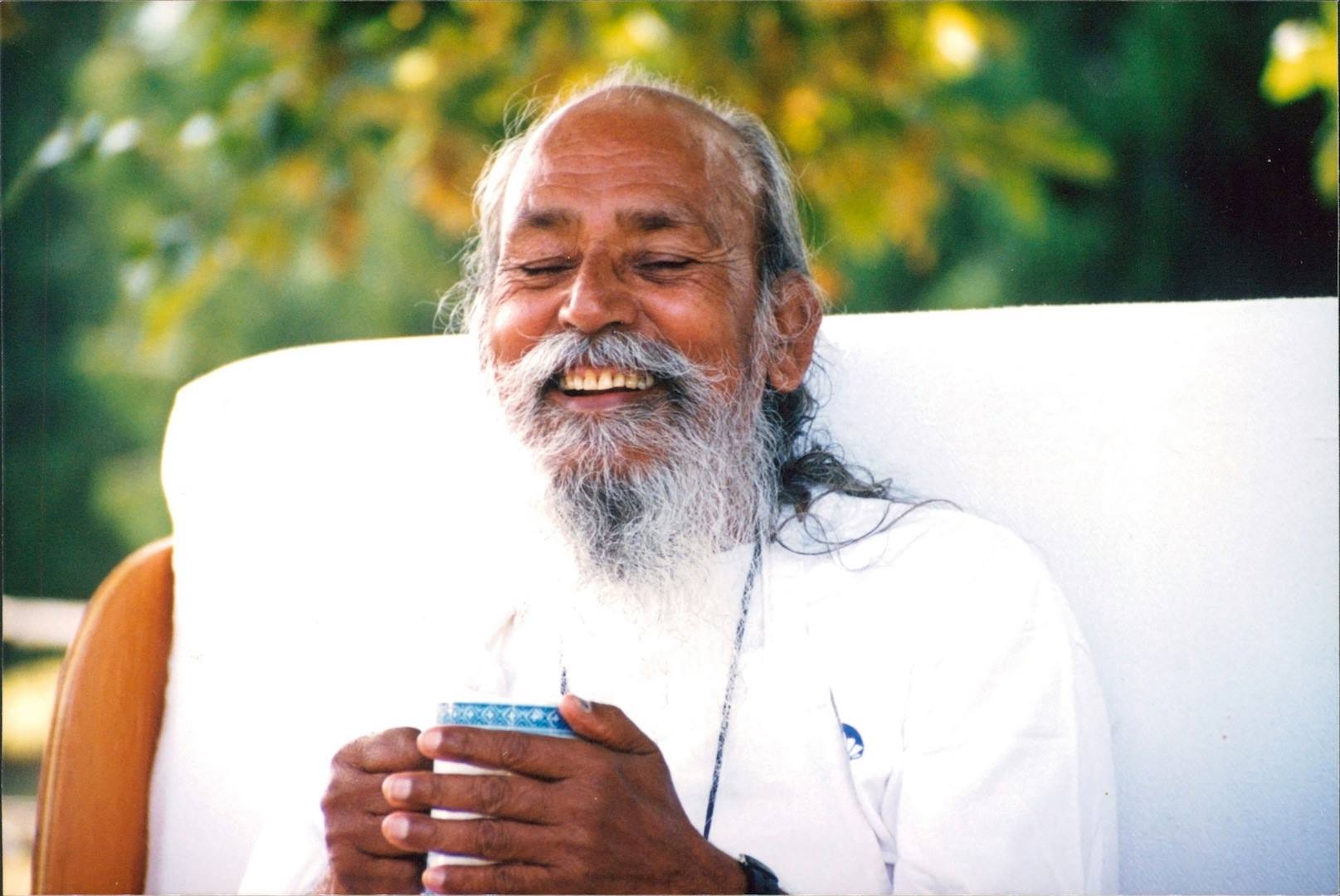 Babaji laughing, eyes closed, holding a cup