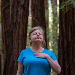 person forest bathing standing in the redwoods with hand to heart