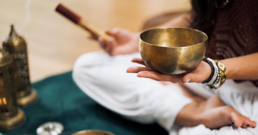 person holding Tibetan singing bowl leading yoga and sound healing class