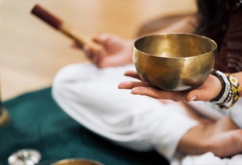 person holding Tibetan singing bowl leading yoga and sound healing class