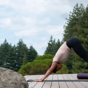 person in mountain pose, doing yoga outside on a deck with redwoods backdrop