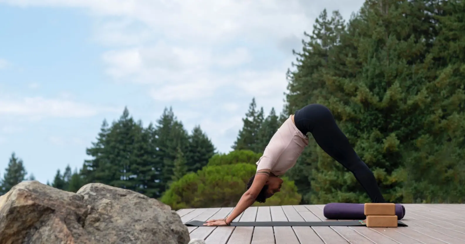 person in mountain pose, doing yoga outside on a deck with redwoods backdrop