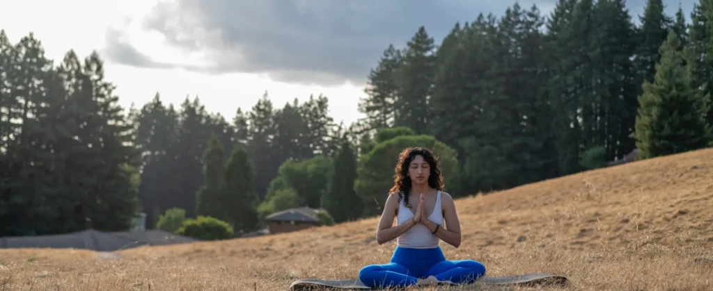 Person sitting in the grass in namaste, photo submitted for USA Today 10Best Awards: Best Yoga Retreat Center & Best Meditation Center