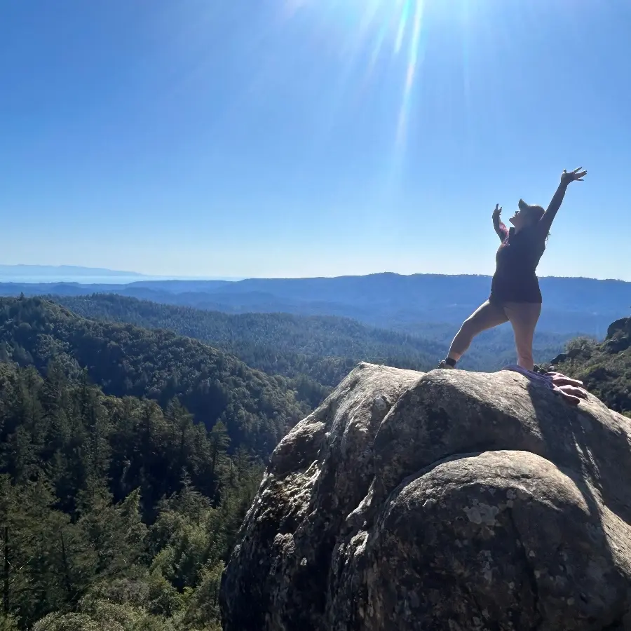 Person standing on a rock overlooking mountains for Women Who Are Up To Something Retreat.