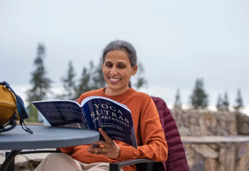 Yoga student smiling while reading The Yoga Sutras of Patanjali outdoors at Mount Madonna's mountaintop retreat center