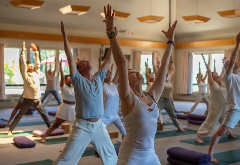 Yoga students practicing standing poses together in Mount Madonna's sunlit mountaintop yoga hall