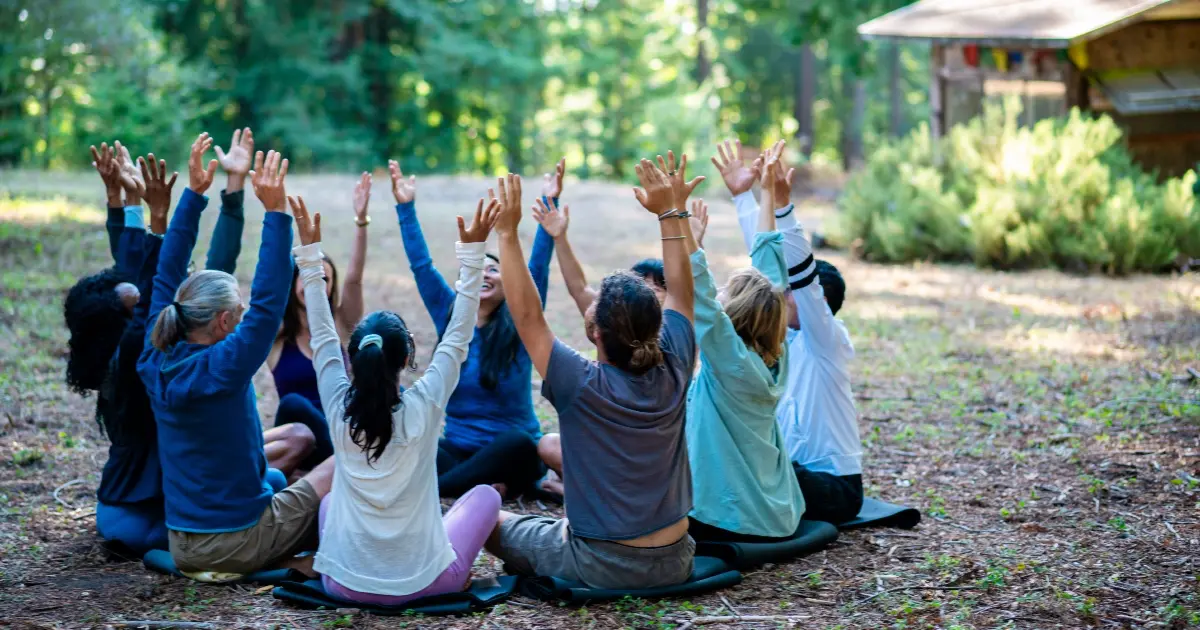 People sitting on the ground in a circle with arms outstretched for Hanuman Fellowship HFS Annual General Meeting at Mount Madonna