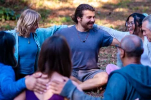 Group of people sitting on the ground, hugging and smiling, at Mount Madonna