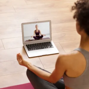 Person sitting on yoga mat with computer for online Hatha Yoga class