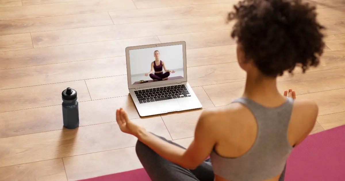 Person sitting on yoga mat with computer for online Hatha Yoga class